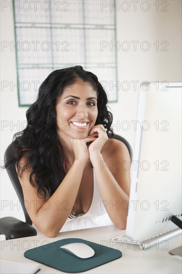 Portrait of smiling Mixed Race woman sitting at desk with computer