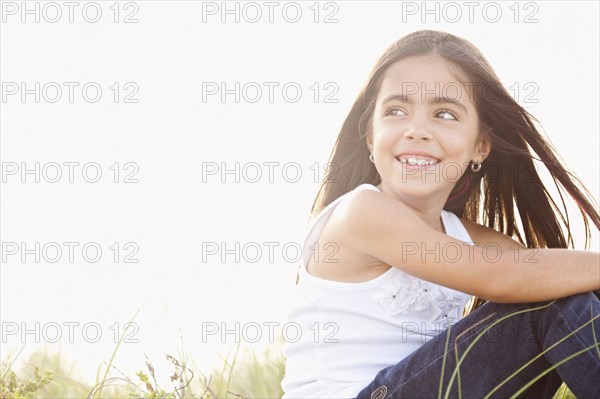 Wind blowing hair of Mixed Race girl sitting in grass