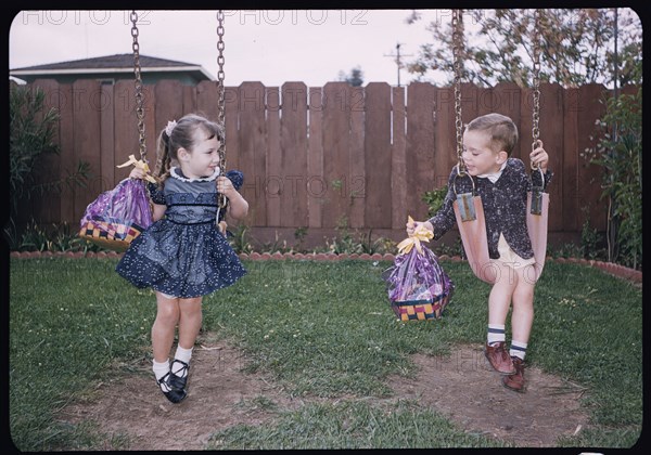 Caucasian brother and sister on swings holding Easter baskets