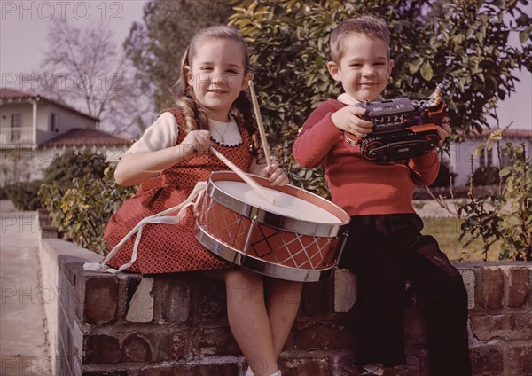 Caucasian brother and sister sitting on brick wall with toys