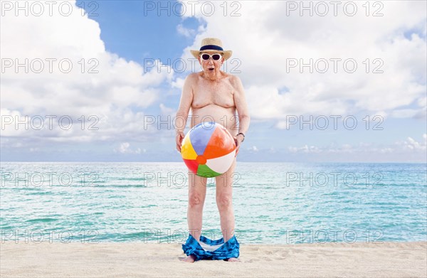 Naked older Caucasian man covering waist with beach ball