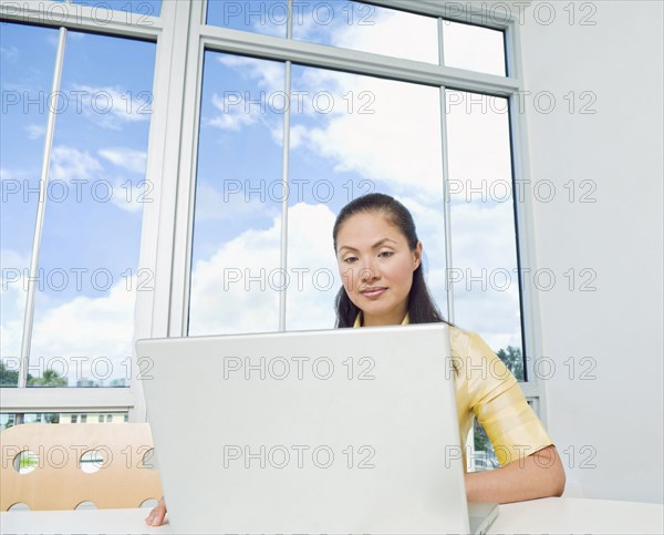 Mixed Race businesswoman using laptop near window
