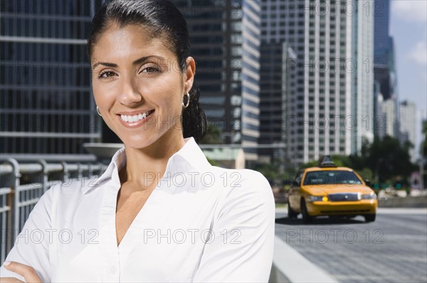 Smiling Mixed Race businesswoman near taxi in city