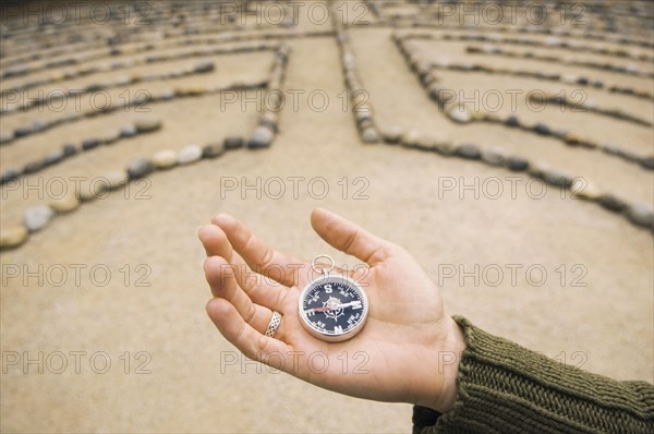 Hand of Mixed Race woman holding compass in maze