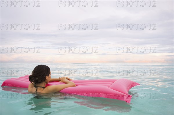 Mixed Race woman floating in ocean on inflatable raft