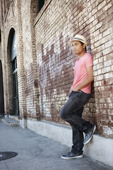 Asian man leaning against brick wall