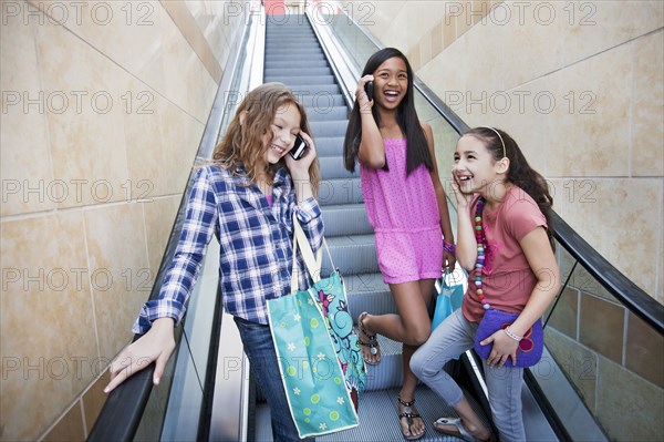 Friends using cell phones on shopping mall escalator