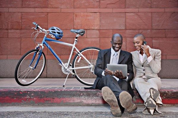 Business people sitting on curb using digital tablet and cell phone