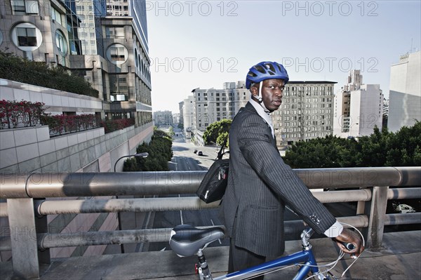 Businessman pushing bicycle over urban bridge