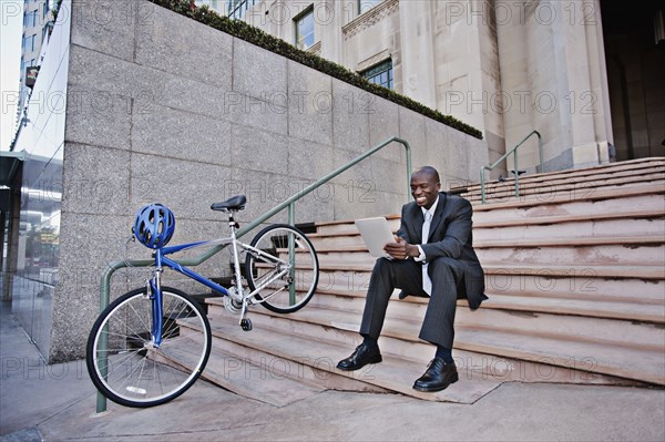 Businessman sitting on stairs using digital tablet