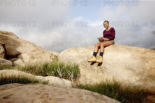 Black woman using digital tablet on rock