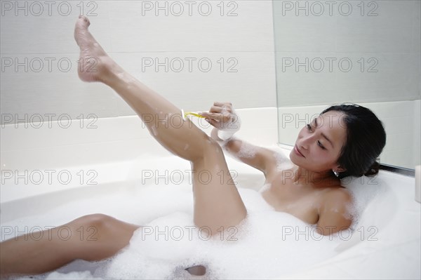 Woman shaving her legs in bubble bath