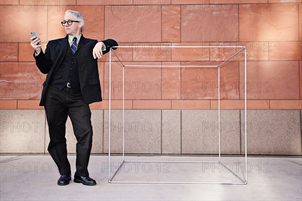 Caucasian businessman leaning on box and text messaging on cell phone