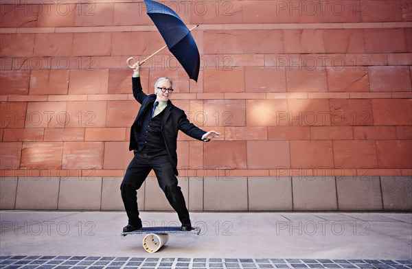 Caucasian businessman holding umbrella and balancing on board