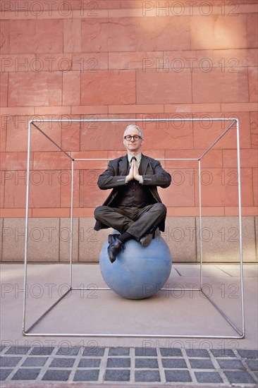 Caucasian businessman practicing yoga on ball inside of box