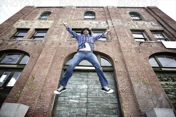 Black man jumping next to urban building