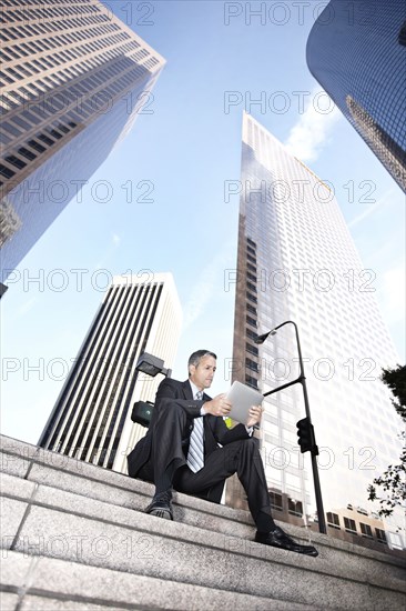 Hispanic businessman sitting on steps with digital tablet