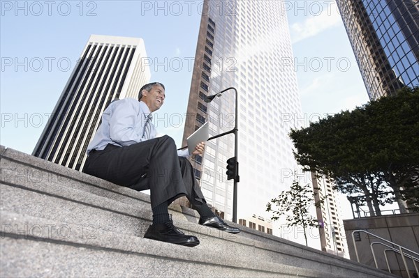 Hispanic businessman sitting on steps with digital tablet