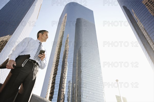 Hispanic businessman holding cell phone and notebook outdoors