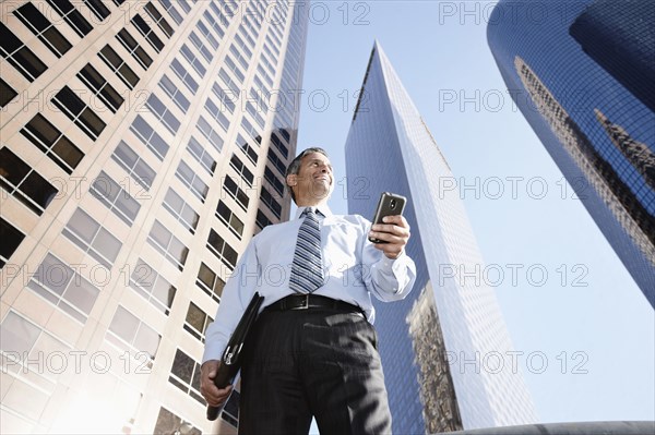 Hispanic businessman holding notebook and cell phone outdoors