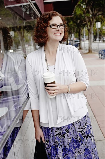 Mixed race woman drinking coffee on sidewalk