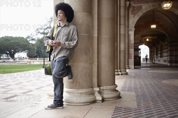 Student with afro leaning against pillar on campus