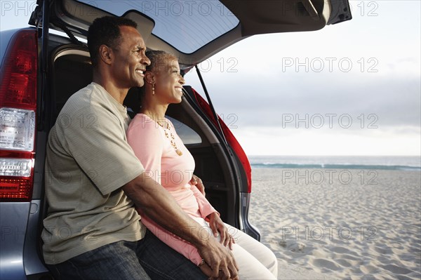 Black couple sitting on hatchback enjoying the beach