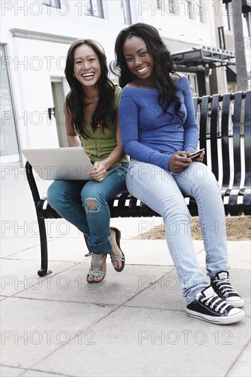 Friends sitting on bench using laptop