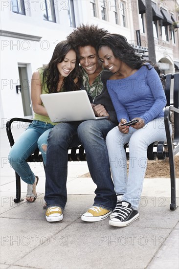 Friends sitting on bench using laptop