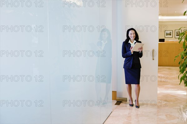 Mixed race businesswoman using digital tablet in office corridor