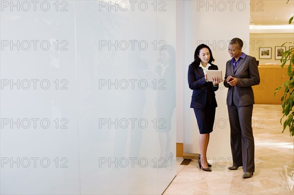 Businesswomen using digital tablet in office corridor