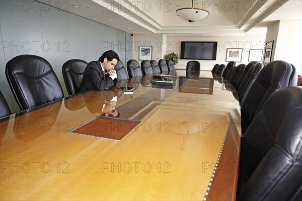 Hispanic businessman sitting in empty conference room