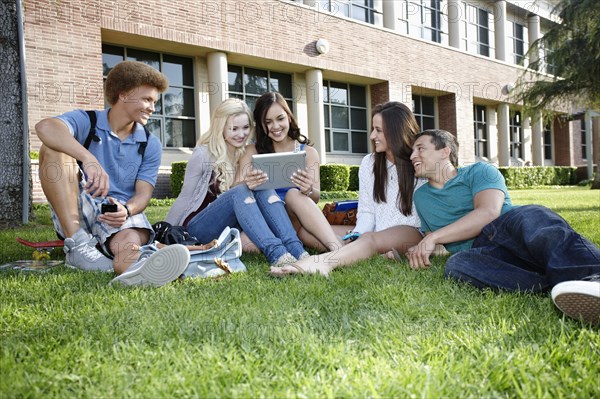 School friends hanging out on grass with digital tablet