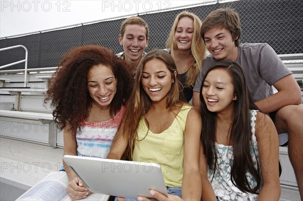 School friends sitting together on bleachers using digital tablet