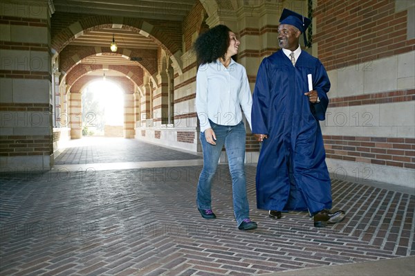 Daughter walking with father in graduation cap and gown