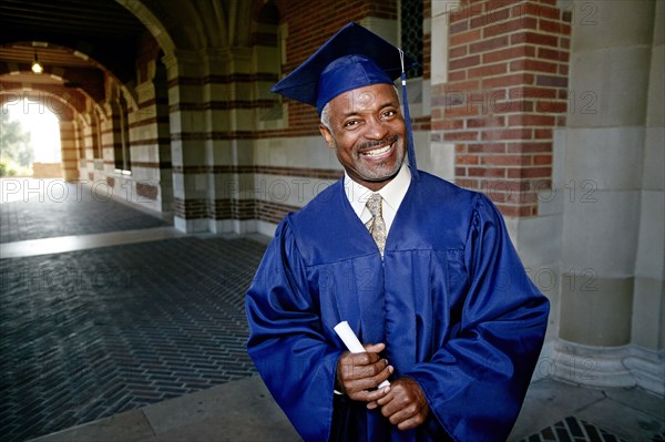 Smiling Black man holding graduation diploma