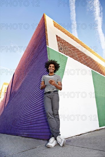 Man using digital tablet and leaning on wall outdoors