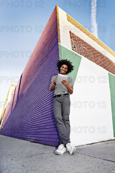 Man using digital tablet and leaning on wall outdoors