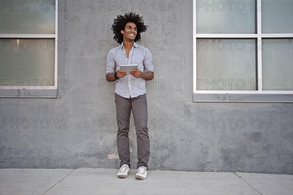 Man using digital tablet and leaning on wall outdoors