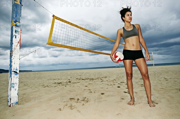 Mixed race woman holding volleyball on beach