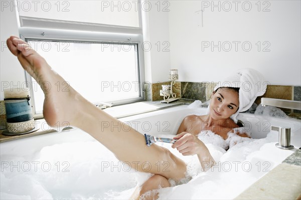 Mixed race woman shaving in bubble bath