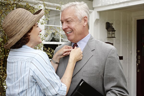 Woman adjusting husband's tie on front path