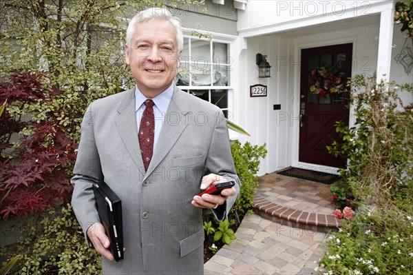 Businessman using cell phone on front path