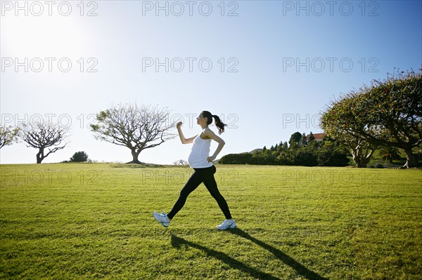 Pregnant mixed race woman exercising in field