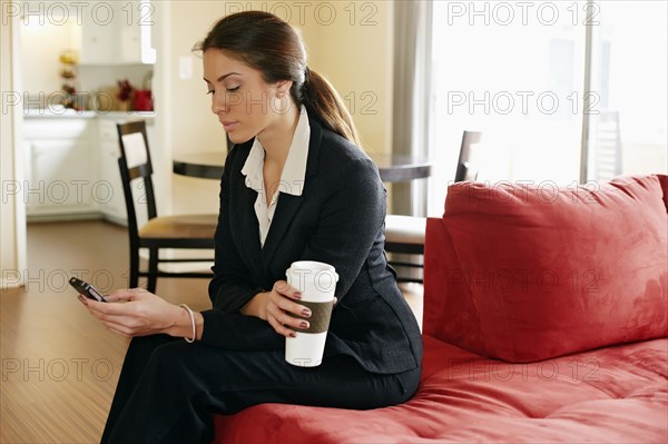 Mixed race businesswoman using cell phone on sofa