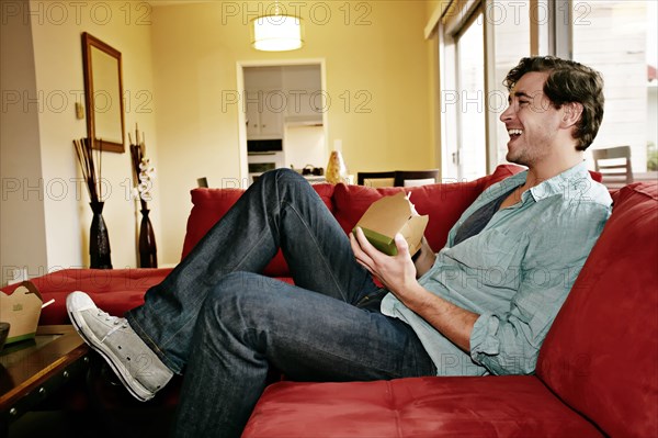 Caucasian man eating take out food on sofa