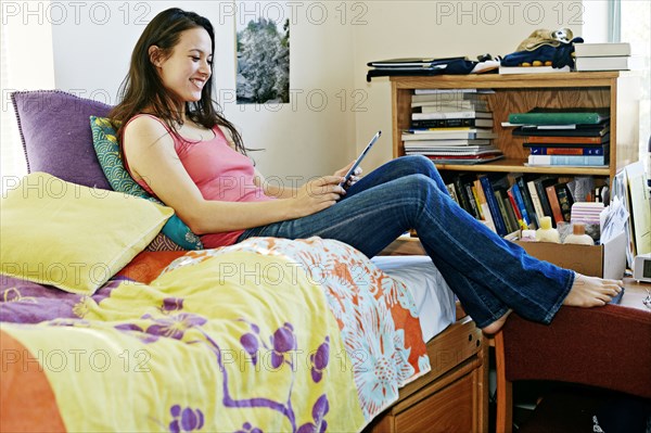 Mixed race college student using tablet computer in dorm