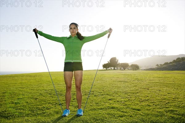 Hispanic woman jumping rope in rural landscape