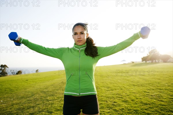 Hispanic woman lifting weights in field