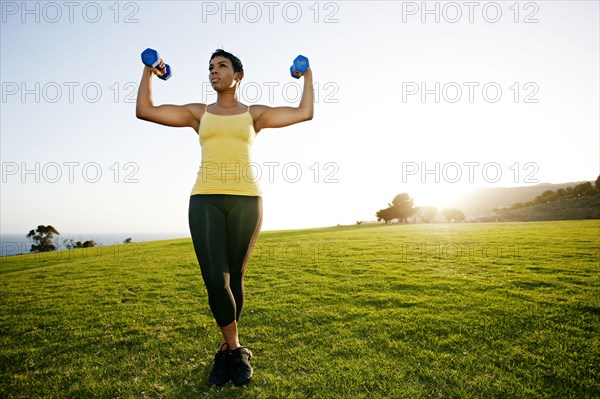 Black woman lifting weights in rural landscape